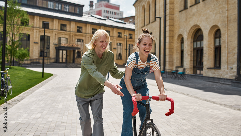 Guy helping excited girl riding bicycle in city