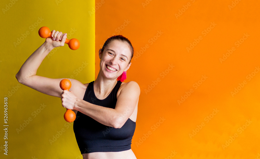 photo happy girl holding orange dumbbells orange and yellow background photo happy girl holding orange dumbbells orange and yellow background
