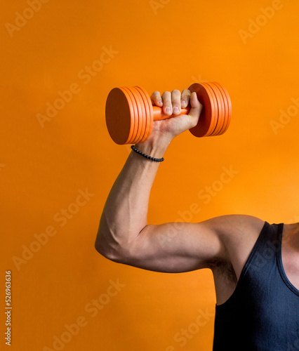 Fototapeta Naklejka Na Ścianę i Meble -  photo of a sporty male torso with dumbbells in hand on an orange background
