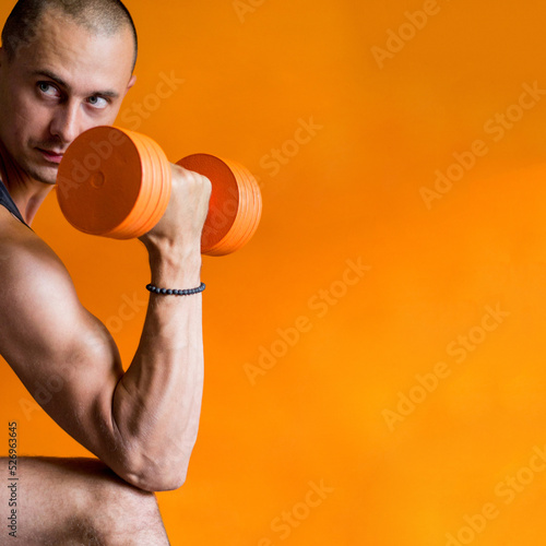 Fotografija photo of a strong and athletic man holding an orange dumbbell in his hand orange