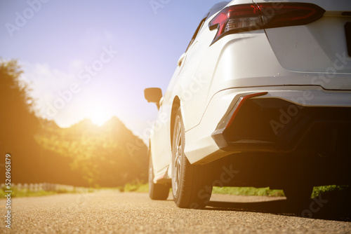 Close-up rear view of a white car with morning light with mountains and sky on the road.