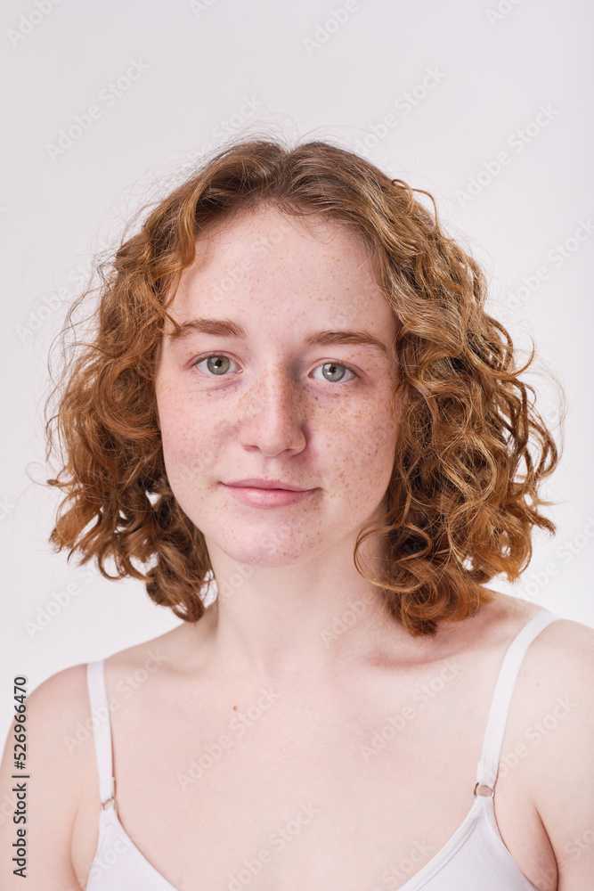 Portrait of red haired girl with curly hair and with freckles on her face looking at camera isolated on white background Portrait of red haired girl with curly hair and with freckles on her face looking at camera isolated on white background