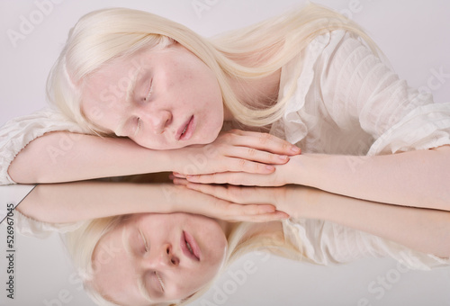 Portrait of albino girl with white hair and eyelashes posing with her eyes closes against white background