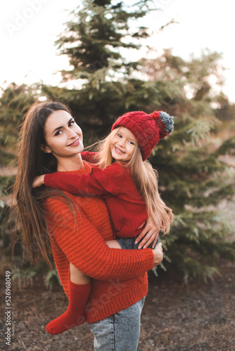 Young woman mom spend time with daughter kid girl wear red knit sweater and hat over tree outdoor. Motherhood. Autumn season. Happiness.