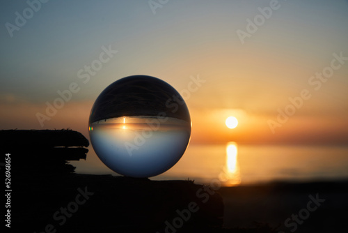 View on a sunset over ocean coast through a glass ball. Selective focus.