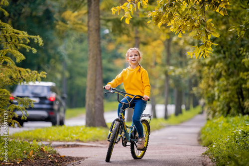 smiling girl of ten in a yellow sweater rides bicycle on autumn street under the branches of a red rowan tree.