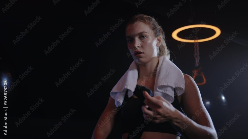 Portrait of the boxer woman binds hand bandage before the training standing in the boxing gym carrying the white towel on her shoulders. People and boxing concept Portrait of the boxer woman binds hand bandage before the training standing in the boxing gym carrying the white towel on her shoulders. People and boxing concept