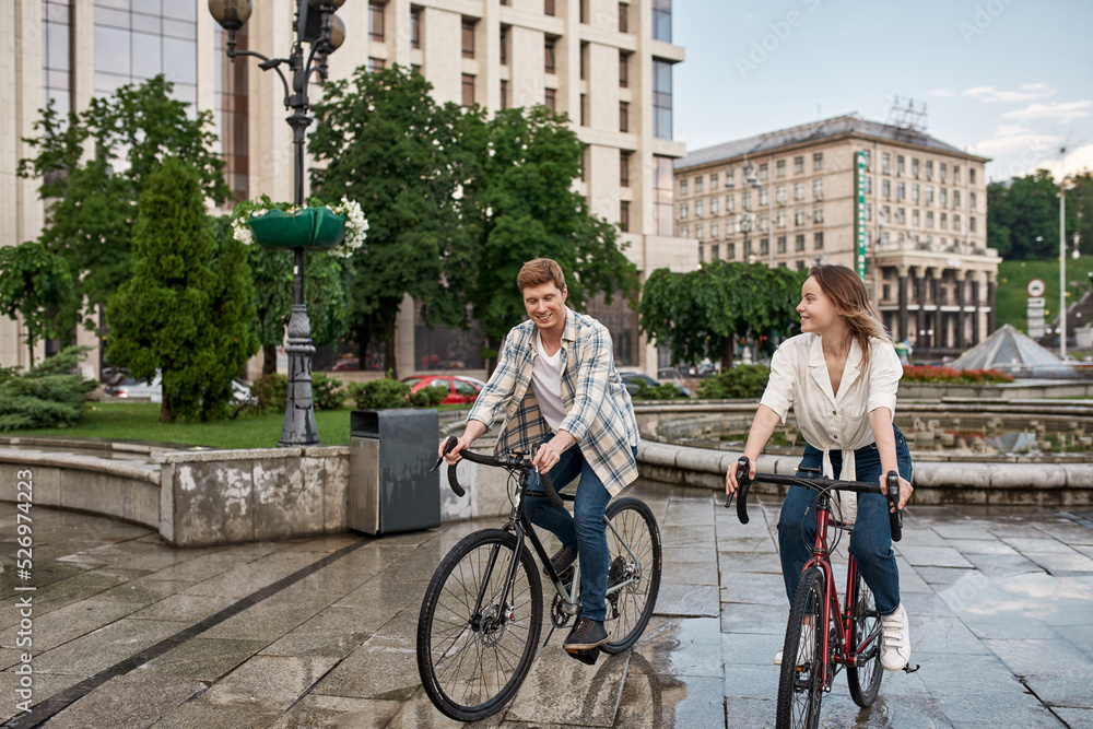 European couple riding bicycles in city after rain