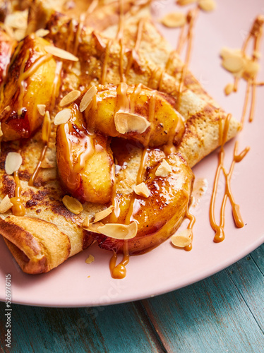 Close up of crepes on a pink plate with cooked apples, almonds and caramel