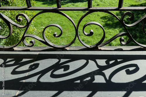 Black iron ornamental banister creating a strong shadow composition of curious spirals with a green grass backgroundas a background