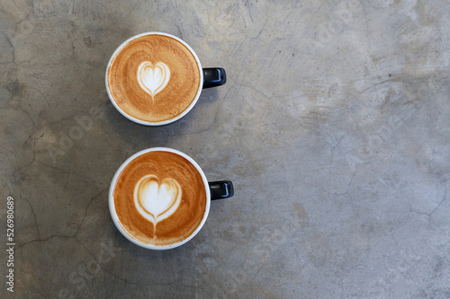 Two hot cups of cappucino on concrete background. Heart shape art latte symbol of love.