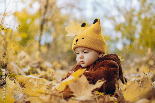 The kid sits in yellow leaves in the park for a walk.