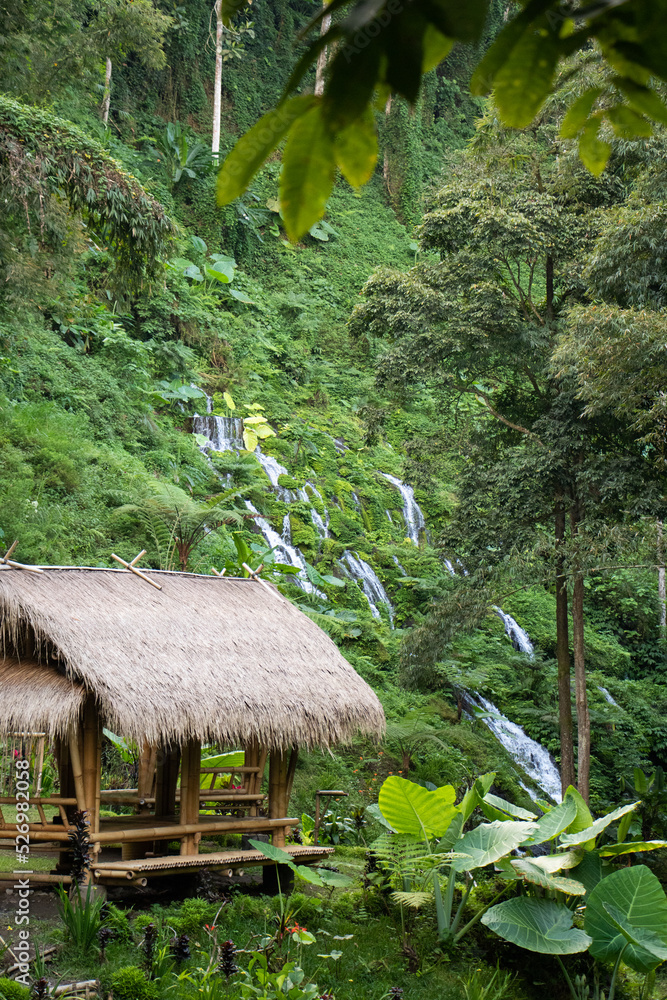 Indonesian hut overlooking beautiful cascading waterfalls on lush hillside in Balinese jungle - Bali, Indonesia Indonesian hut overlooking beautiful cascading waterfalls on lush hillside in Balinese jungle - Bali, Indonesia