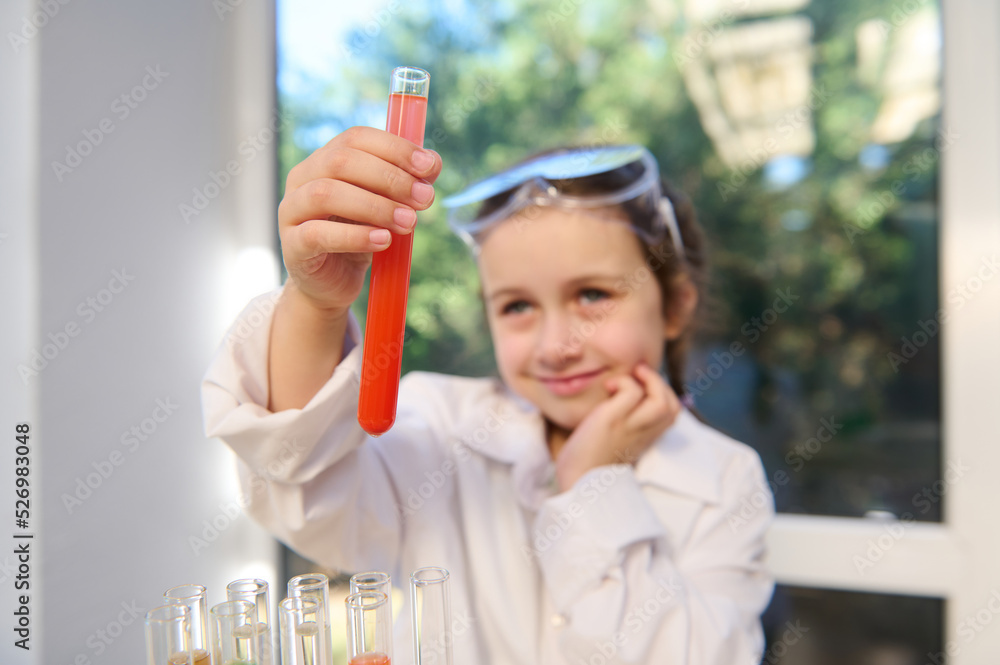 Details: hands of a little girl wearing protective workwear and safety lab goggles, future chemist scientist observing the test tube with going chemical reaction with fascination and excitement Details: hands of a little girl wearing protective workwear and safety lab goggles, future chemist scientist observing the test tube with going chemical reaction with fascination and excitement