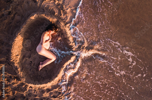 Mujer embarazada tumbada en la arena simulando un útero y el cordón umbilical.  photo