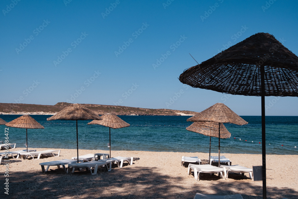 straw umbrellas and sunbeds on the beach near the blue waves on sea with the view of island