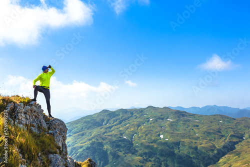 a male climber on the edge of a cliff over a abyss looks into the distance over mountain ranges and the blue summer sky