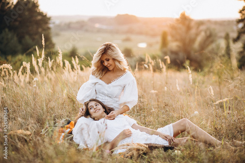 Mother and teenage daughter together in white dresses in the meadow