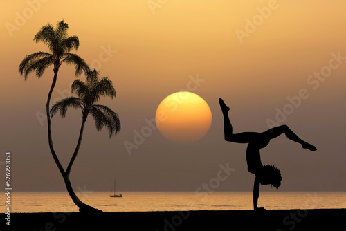 Photography Silhouette of young woman practicing yoga near the ocean with tropical sunset ba