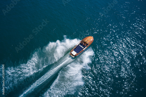Expensive wooden classic italian boat with people moving faster on dark blue water top view. Fast moving expensive modern wooden boats aerial view.