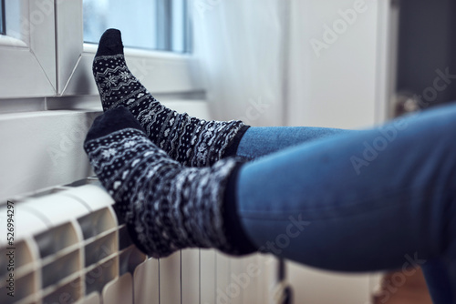Woman heating feet on a chilly winter day, energy and gas crisis, cold room, heating problems. photo