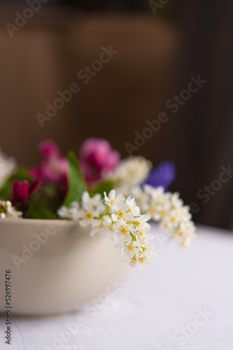 Spring blooming delicate flowers in a round vase on a table with a white tablecloth  a pastel bouquet and a delicate floral card 