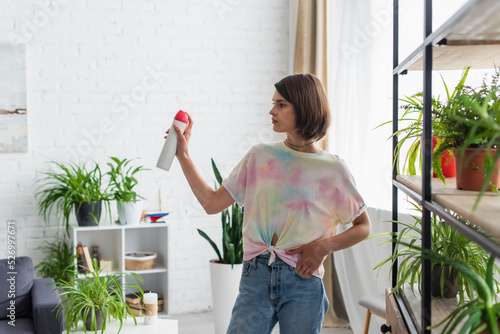 Young woman spraying air freshener while standing in living room. photo