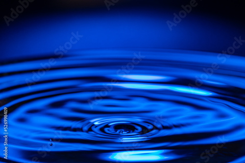 Macro water drop on a blue background and circles on it. Round water drop. Drops, splashes, spray, abstract shapes out of the water