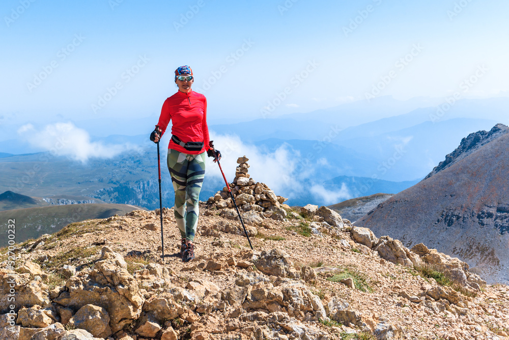 Obraz premium a female climber conquers the peak against the background of the blue sky enters the mountain with trekking poles