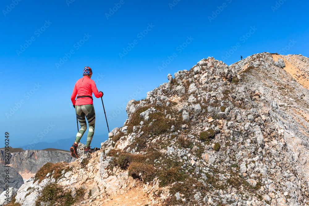 a female climber conquers the peak against the background of the blue sky enters the mountain with trekking poles