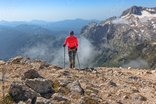 a female climber conquers the peak against the background of the blue sky enters the mountain with trekking poles