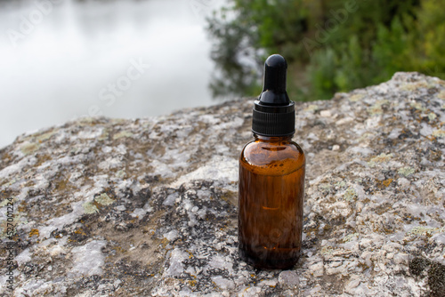 Amber glass dropper bottle of face serum or essential oil on granite stone rock textured background outdoor over the river. Natural organic spa cosmetic concept. Top view, copy space