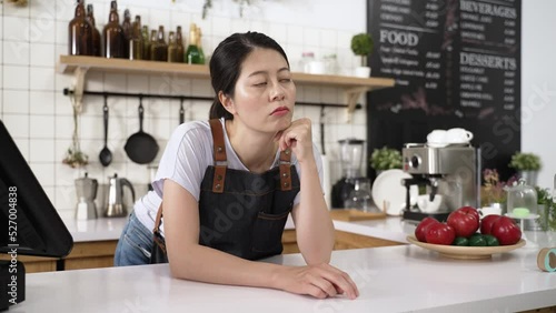 portrait of a bored asian waitress tapping finger and propping head on the counter while waiting for clients to visit the restaurant during pandemic outbreak