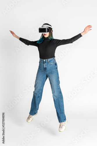 Virtual reality. A teenage girl with blue hair wearing virtual reality glasses watching movies or playing video games jumps, waving her arms. Funny girl looking into VR glasses levitation