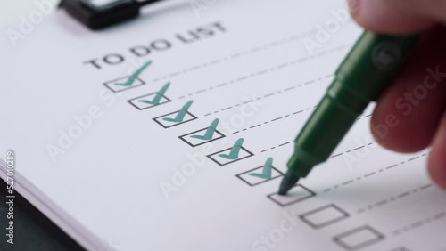 Extreme close up businessman hand marking or tick off with green pen on check list, checkbox, to do list box after completing task on white paper. Selective focus 4K resolution. Checklist and To Do Li photo