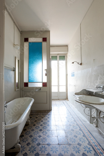 Old bathroom with outdoor bathtub, exposed pipes, and black and white tiles