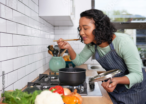 Foto A young multi-racial woman smells and tastes her cooking on the stove