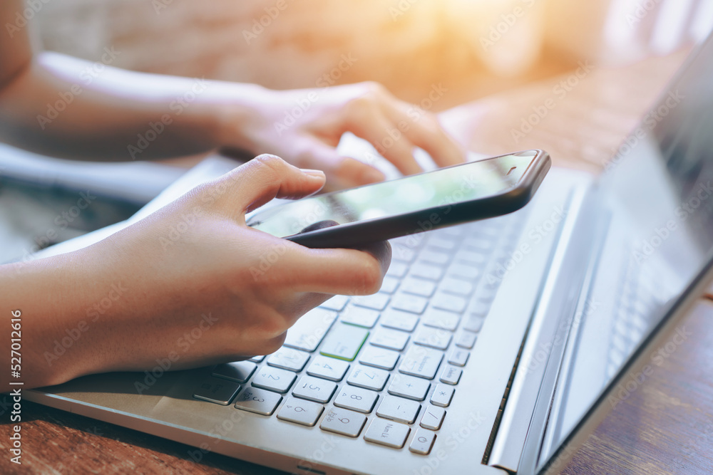 hand of person using smartphone with laptop on wooden table hand of person using smartphone with laptop on wooden table