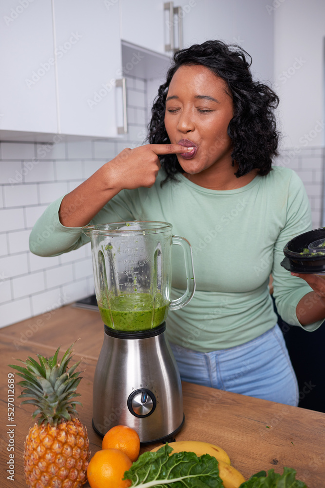 A young multi-ethnic woman tastes her freshly made green smoothie in the kitchen A young multi-ethnic woman tastes her freshly made green smoothie in the kitchen