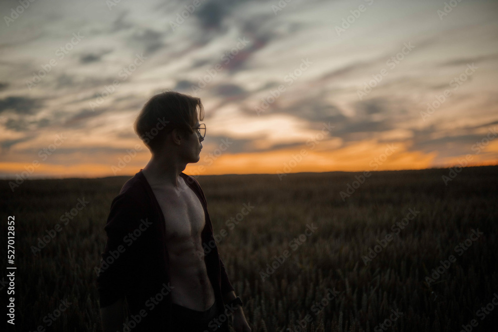 sexy man in a cardigan on a naked body with a rounded torso at sunset in a field. sexy man in a cardigan on a naked body with a rounded torso at sunset in a field.