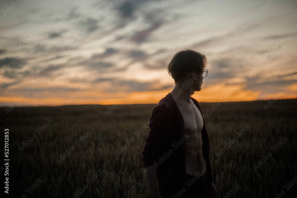 sexy man in a cardigan on a naked body with a rounded torso at sunset in a field. sexy man in a cardigan on a naked body with a rounded torso at sunset in a field.