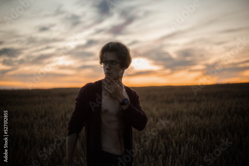sexy man in a cardigan on a naked body with a rounded torso at sunset in a field. © velimir