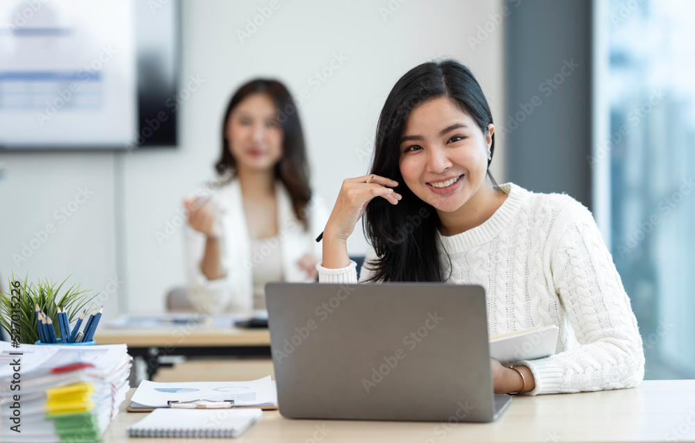 Smiling Asian businesswoman working with a laptop at the office. Looking at the camera. Smiling Asian businesswoman working with a laptop at the office. Looking at the camera.