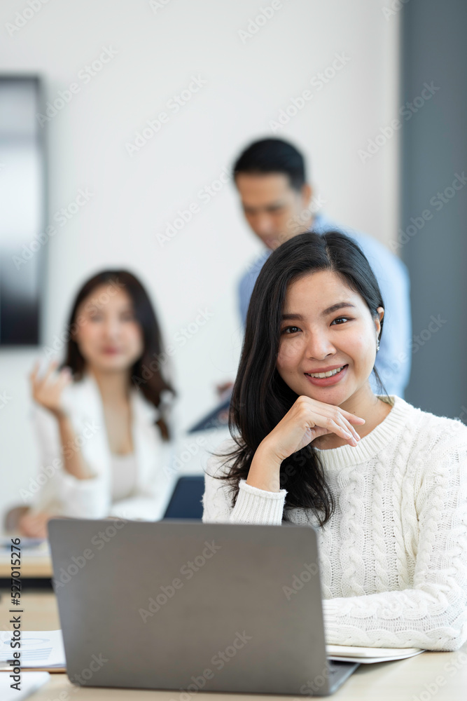 Smiling Asian businesswoman working with a laptop at the office. Looking at the camera. Smiling Asian businesswoman working with a laptop at the office. Looking at the camera.