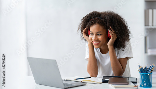 African female student wearing headphones and smiling and using laptop while studying online
