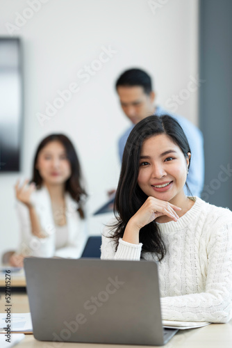 Smiling Asian businesswoman working with a laptop at the office. Looking at the camera.