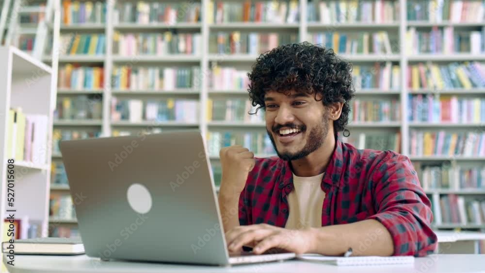 Amazed happy excited stylish mixed race guy, student, sitting in university library with laptop, rejoices in success, win, good mark on the exam, gesturing hands, smiling, emotional face expression Amazed happy excited stylish mixed race guy, student, sitting in university library with laptop, rejoices in success, win, good mark on the exam, gesturing hands, smiling, emotional face expression