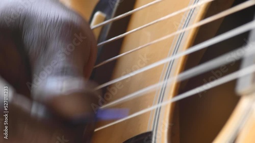 Close shot of black man playing acoustic guitar sitting on chair