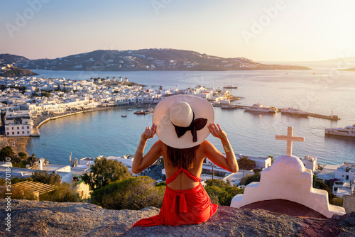 Print op canvas A elegant tourist woman in a red dress enjoys the view over the city of Mykonos