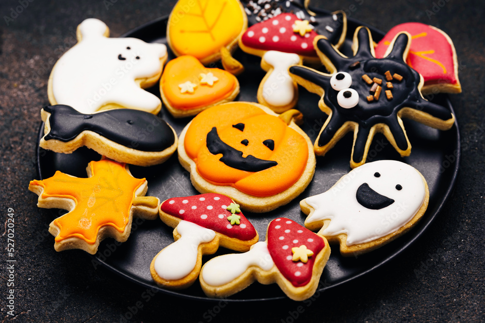Halloween sugar cookies with glase on dark brown background - pumpkin jack, mushrooms, black cat, ghosts, spider, bat. Close up